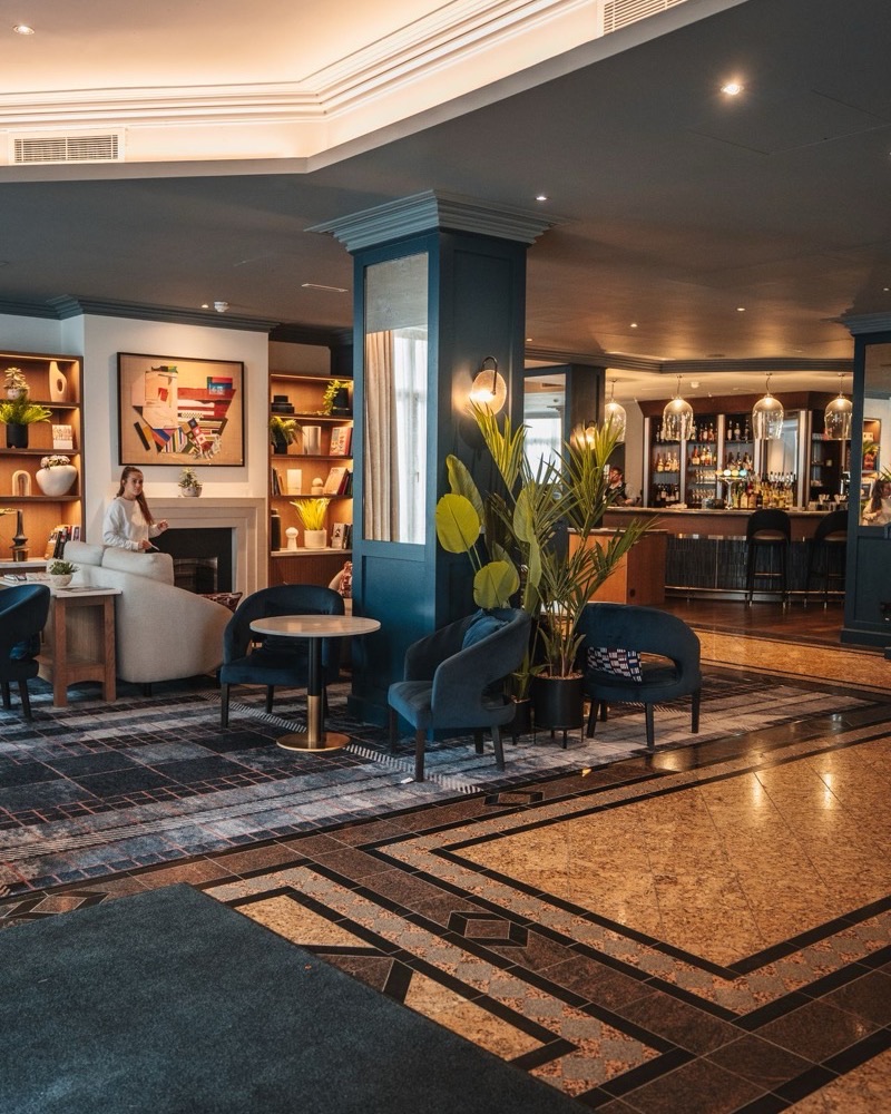 Lobby de hotel com poltronas e bar ao fundo